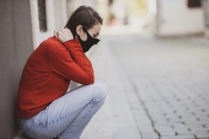 a sad and depressed woman putting on a face mask and sitting down 